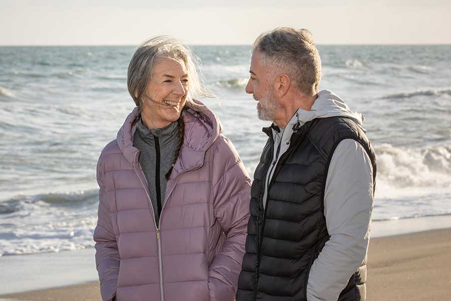 elder couple smiling at beach with coats on