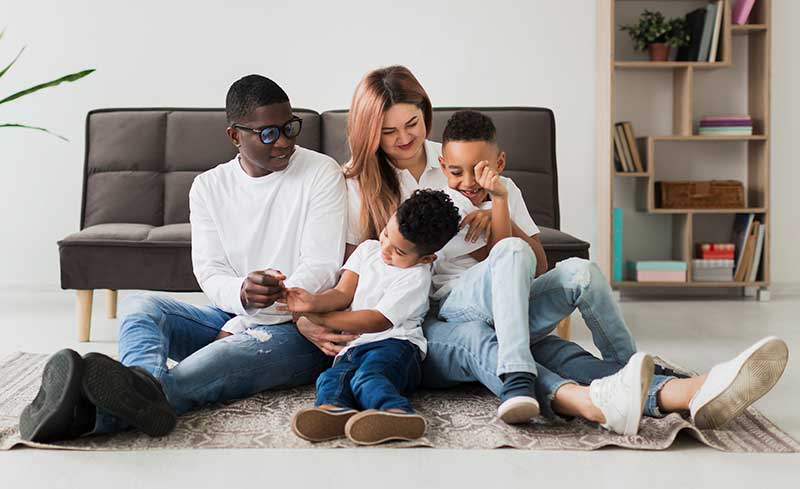 Happy african american family watering plants together in garden. family, love and togetherness concept, unaltered. Multicultural family sitting on family room floor
