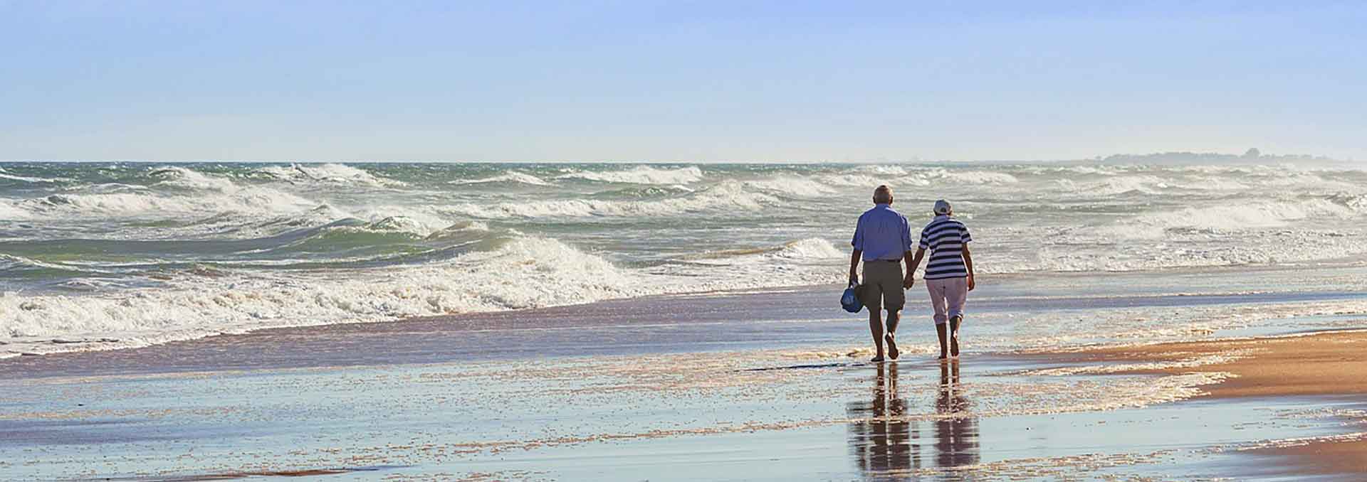 Agent explaining medicare insurance plans Elder couple holding hands walking on beach
