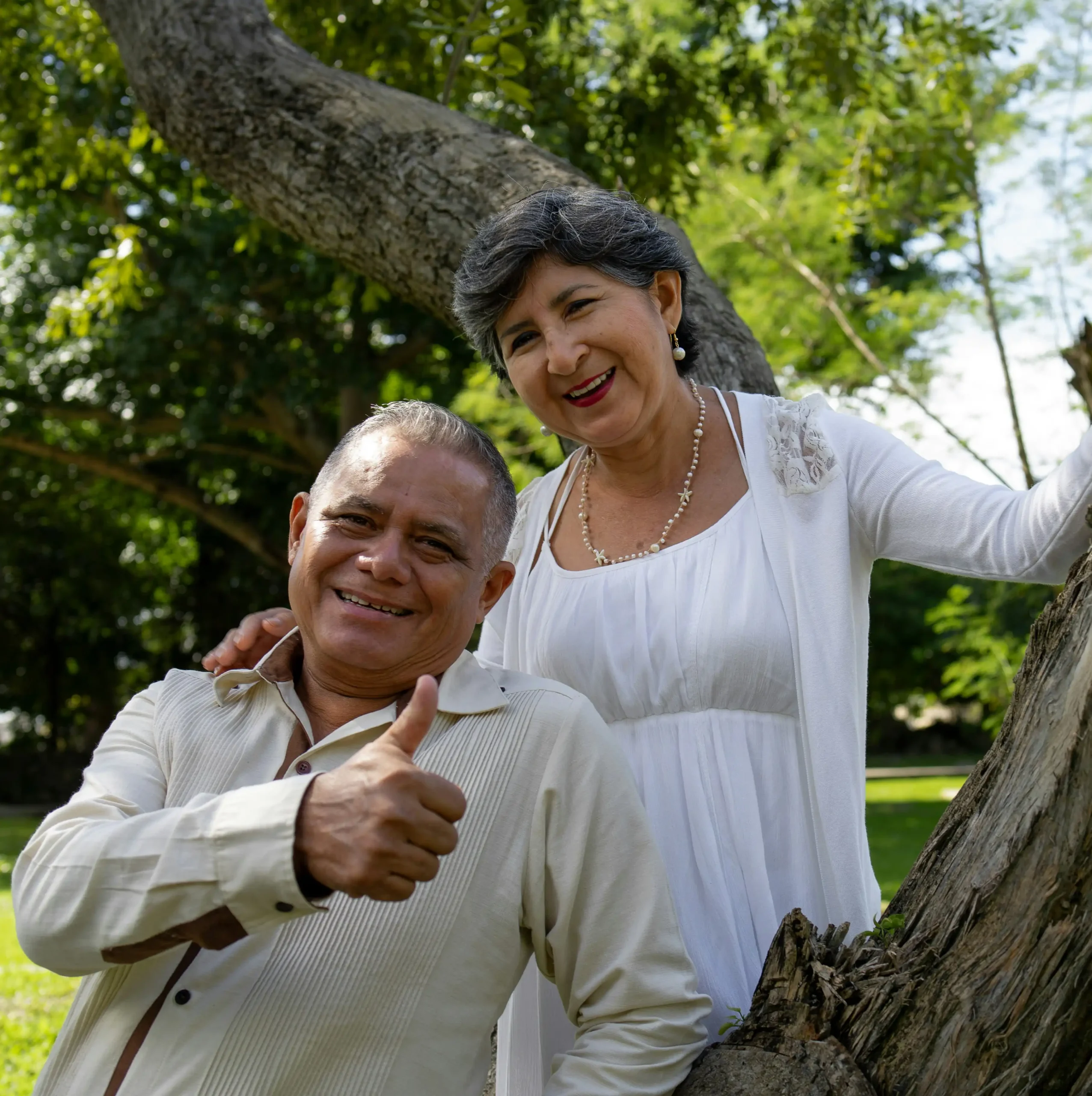 Couple sitting by tree giving thumbs up